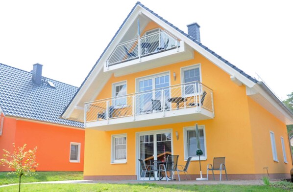A two-story house with a balcony, a small patio with chairs, and a visible chimney.