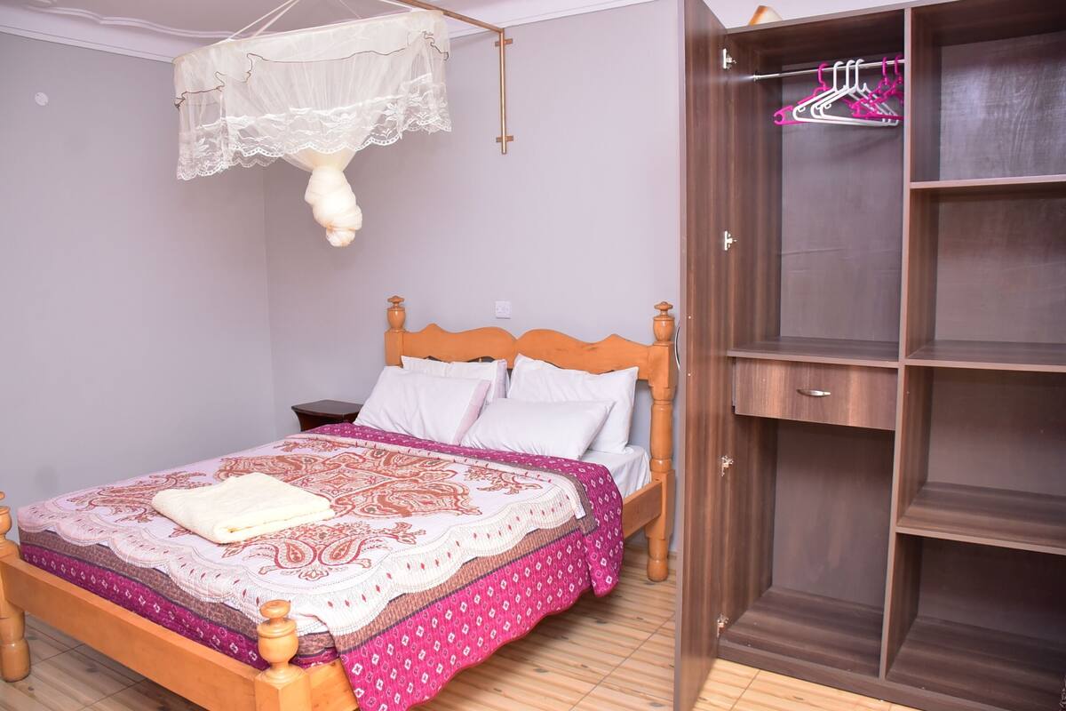 Un dormitorio con cama de madera, mesita de noche, armario y mosquitera colgada.
