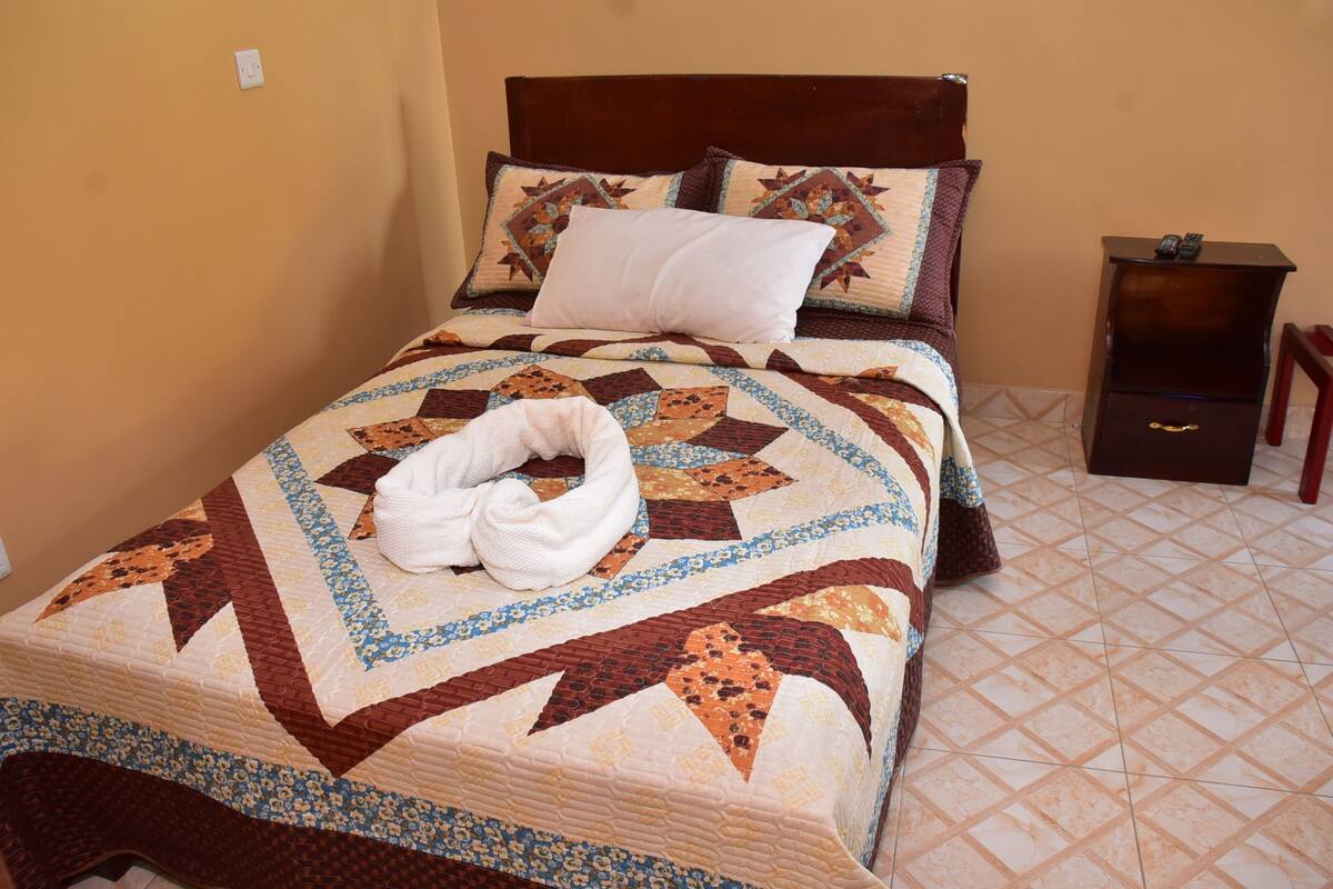 Una cama bien hecha con un edredón estampado, una almohada blanca y una toalla blanca sobre la cama.
