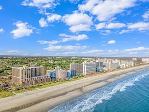 A coastal hotel area with multiple high-rise buildings, a sandy beach, and a view of the ocean.