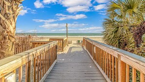 Un paseo marítimo de madera que conduce a una playa bajo un cielo despejado.