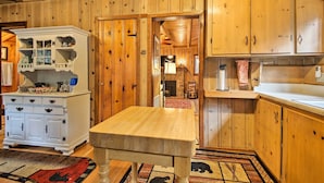A wooden interior with a dining table, a white cabinet with glass doors, and a kitchen area with wooden cabinets and a countertop. - Vintage 'Snow White' Cottage ~ 2 Miles to Village! (Lake Arrowhead)