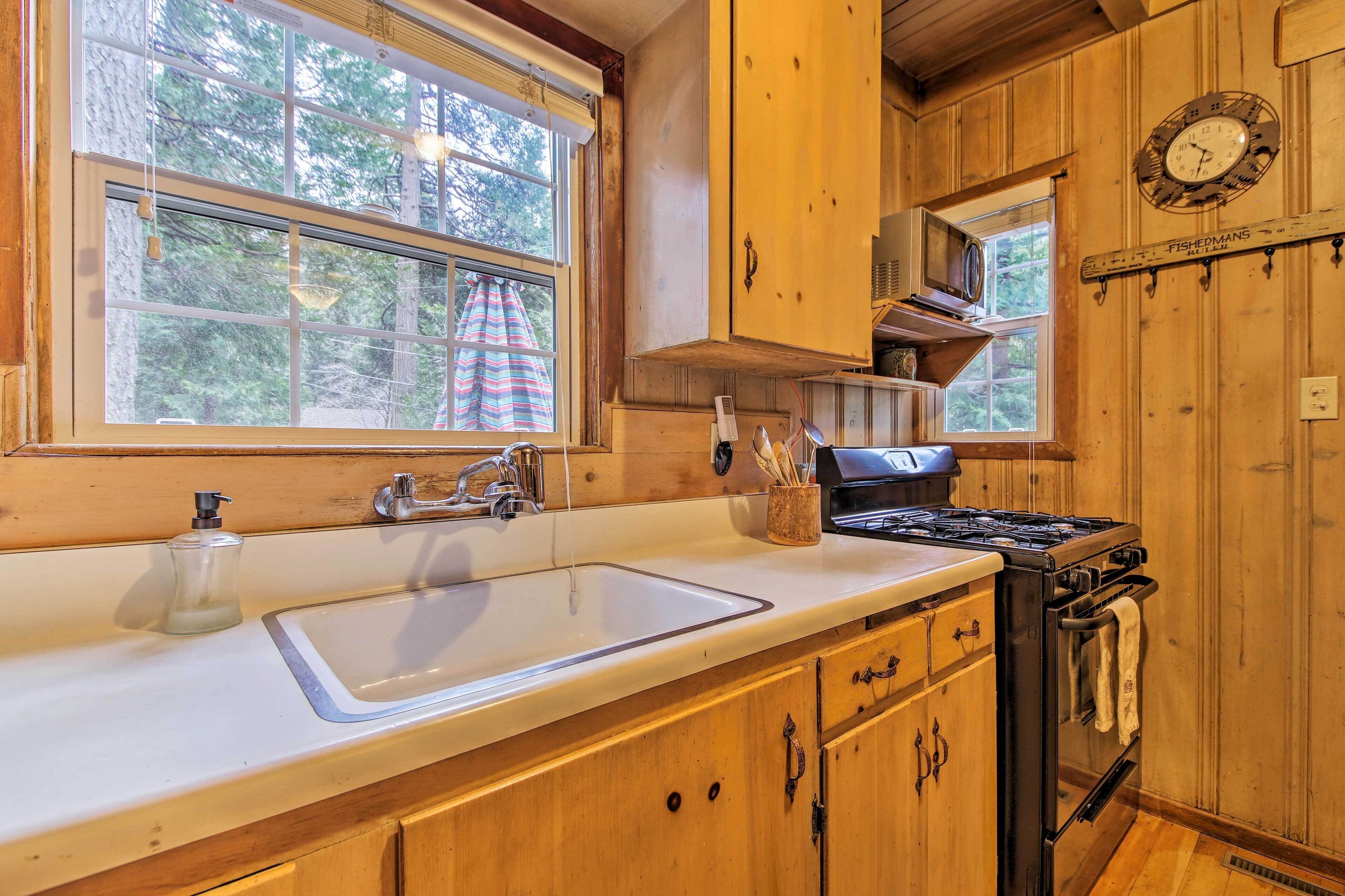Una cocina con gabinetes de madera, un fregadero, una estufa y una ventana con vista a árboles.