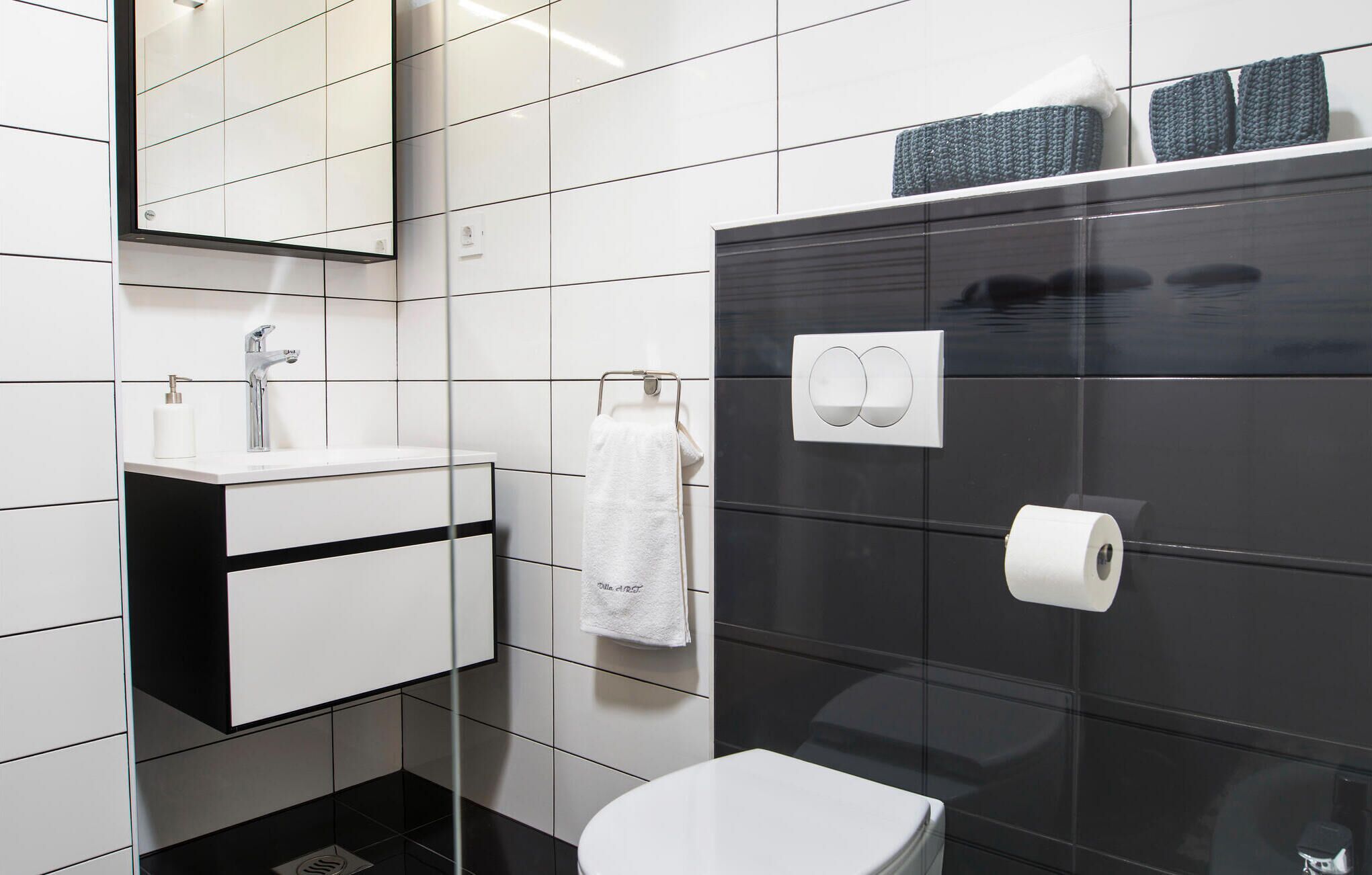 A modern bathroom with a white sink, a mirror, a toilet, and a black tiled wall.
