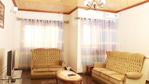 A living room with two beige sofas, a glass coffee table, a television, and a ceiling fan. - Deutch' Lodges (Yaoundé)