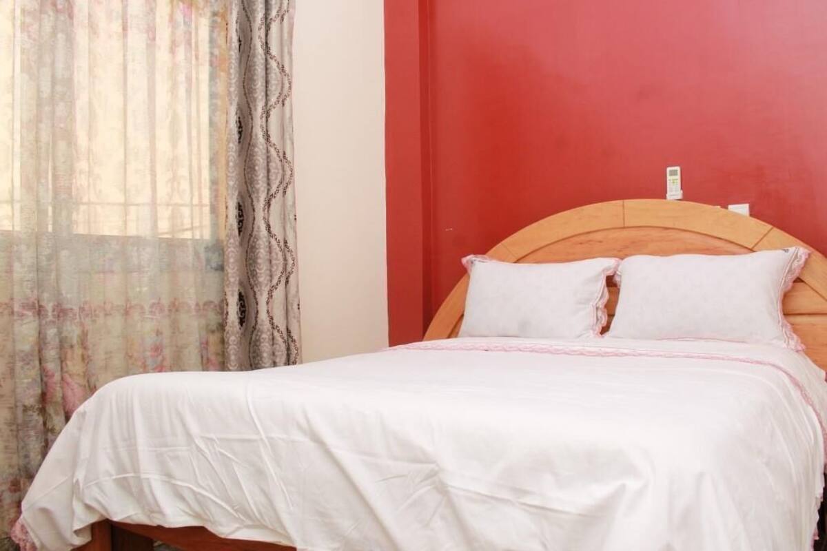 A single bed with a wooden headboard, white bedding, and a red wall.