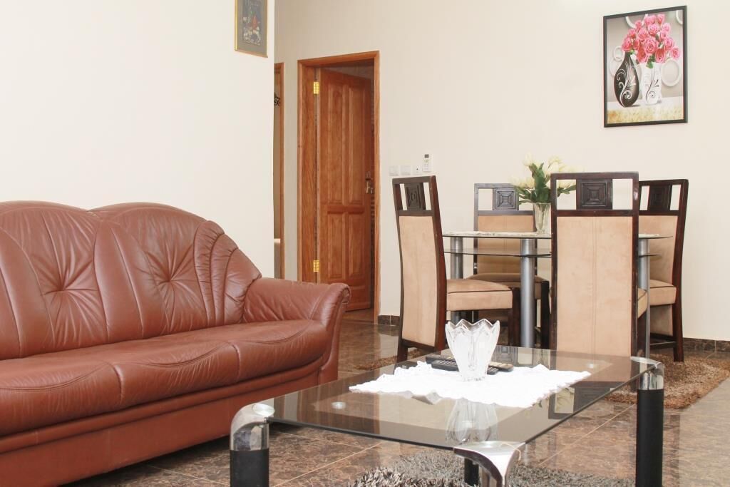 A living room with a brown leather sofa, a glass coffee table, and a dining area with a wooden table and chairs.