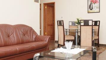 A living room with a brown leather sofa, a glass coffee table, and a dining area with a wooden table and chairs.