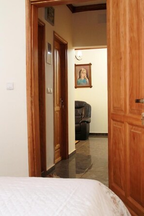 A hallway with a bed at the end, a door, a framed picture on the wall, and a leather chair.