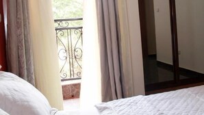 A bedroom with a bed, curtains, and a view of a balcony. - Deutch' Lodges (Yaoundé)