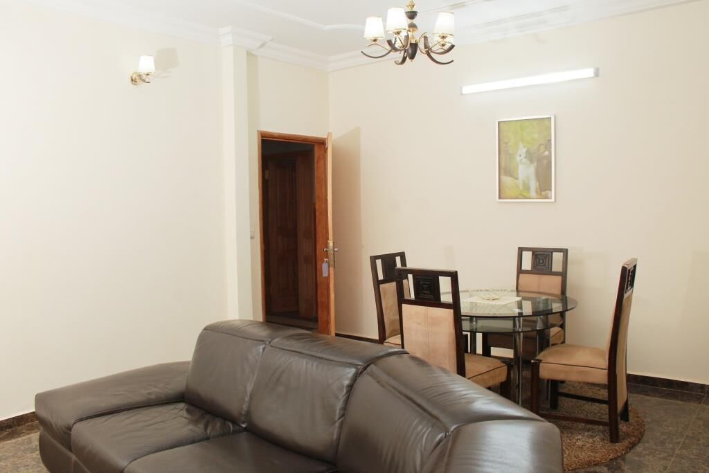 Un salon avec un canapé en cuir, une table à manger en verre entourée de chaises, un lustre et un tableau accroché au mur.
