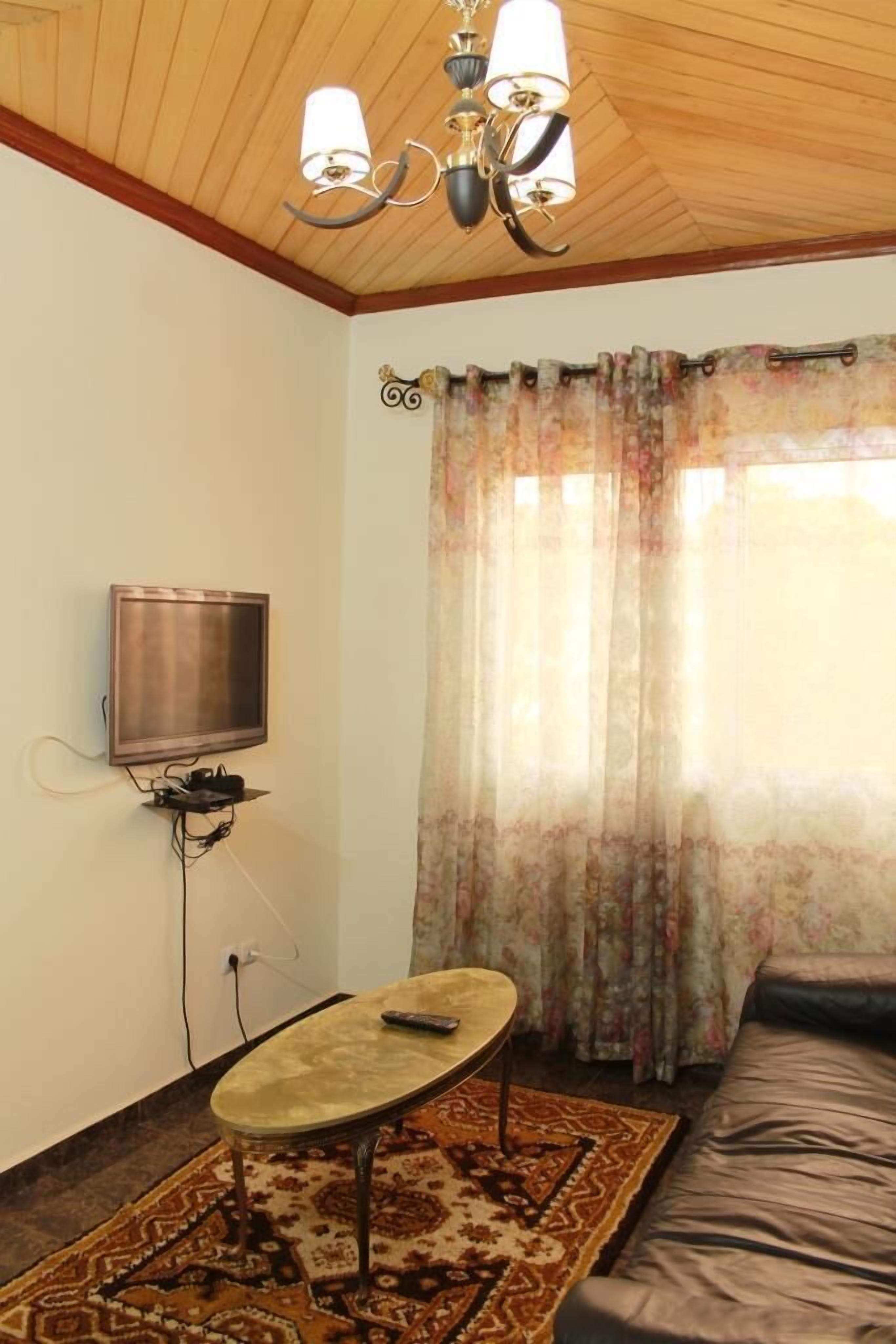 A living room with a television mounted on the wall, a small table, a sofa, and a patterned rug.