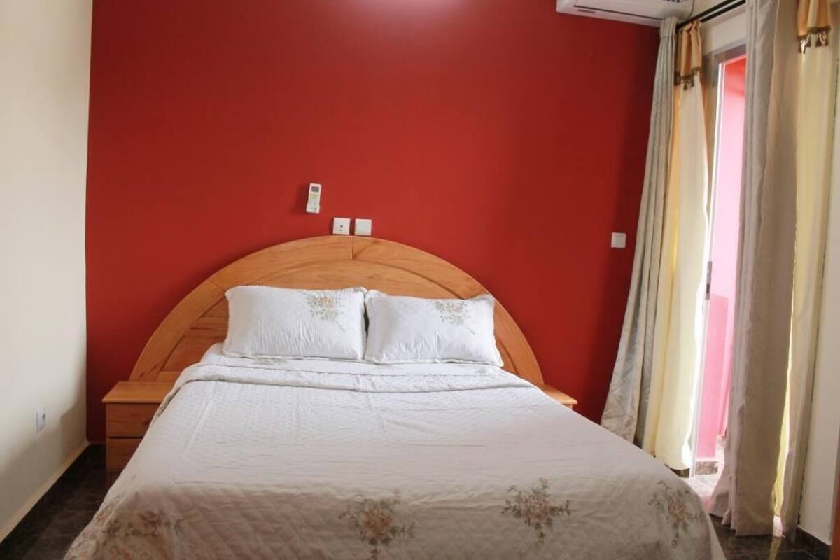 A bedroom with a wooden headboard, a white bedspread, and a red wall.