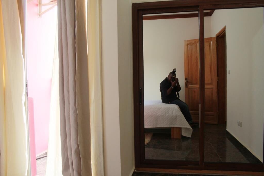 Une pièce dotée d’une porte coulissante, d’un lit recouvert d’une courtepointe blanche et, au fond, d’une porte en bois.