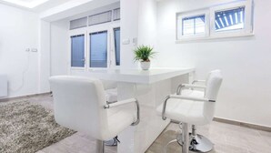 Una habitación moderna y luminosa con una zona de bar blanca, dos taburetes de bar blancos, una planta en maceta y un ventanal con persianas.