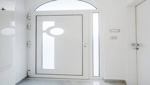 Un pasillo con una puerta blanca que tiene un ventanal circular, un interruptor de luz y un termostato en la pared.