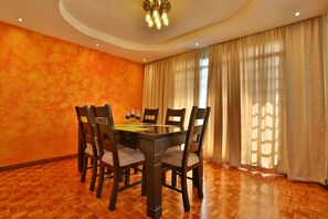 A dining room with a wooden table and chairs, a chandelier, and large windows with curtains. - Shallydeck P'house is a home away from home located in the leafy Nairobi suburb. (Nairobi)