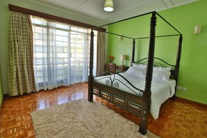 A four-poster bed in a room with green walls, wooden flooring, and a large window with curtains. - Shallydeck P'house is a home away from home located in the leafy Nairobi suburb. (Nairobi)
