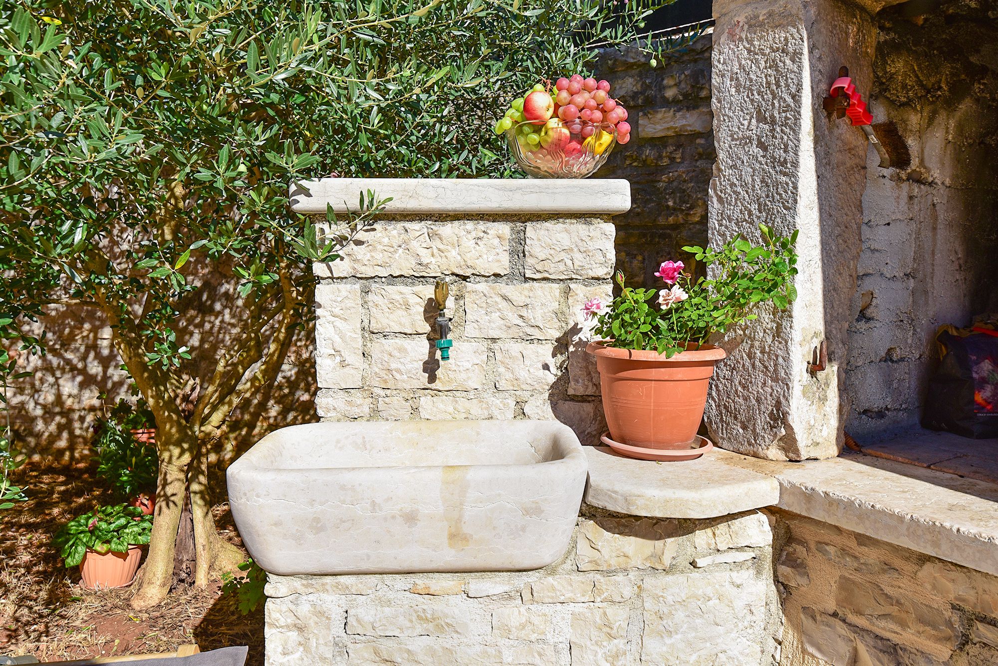 A stone wall with a stone basin, a potted plant, and a bowl of fruit.