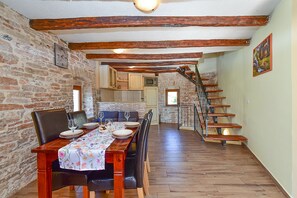 Un coin repas avec une table en bois dressée pour quatre personnes, bordé de murs en briques et agrémenté d’un escalier menant à un niveau supérieur.