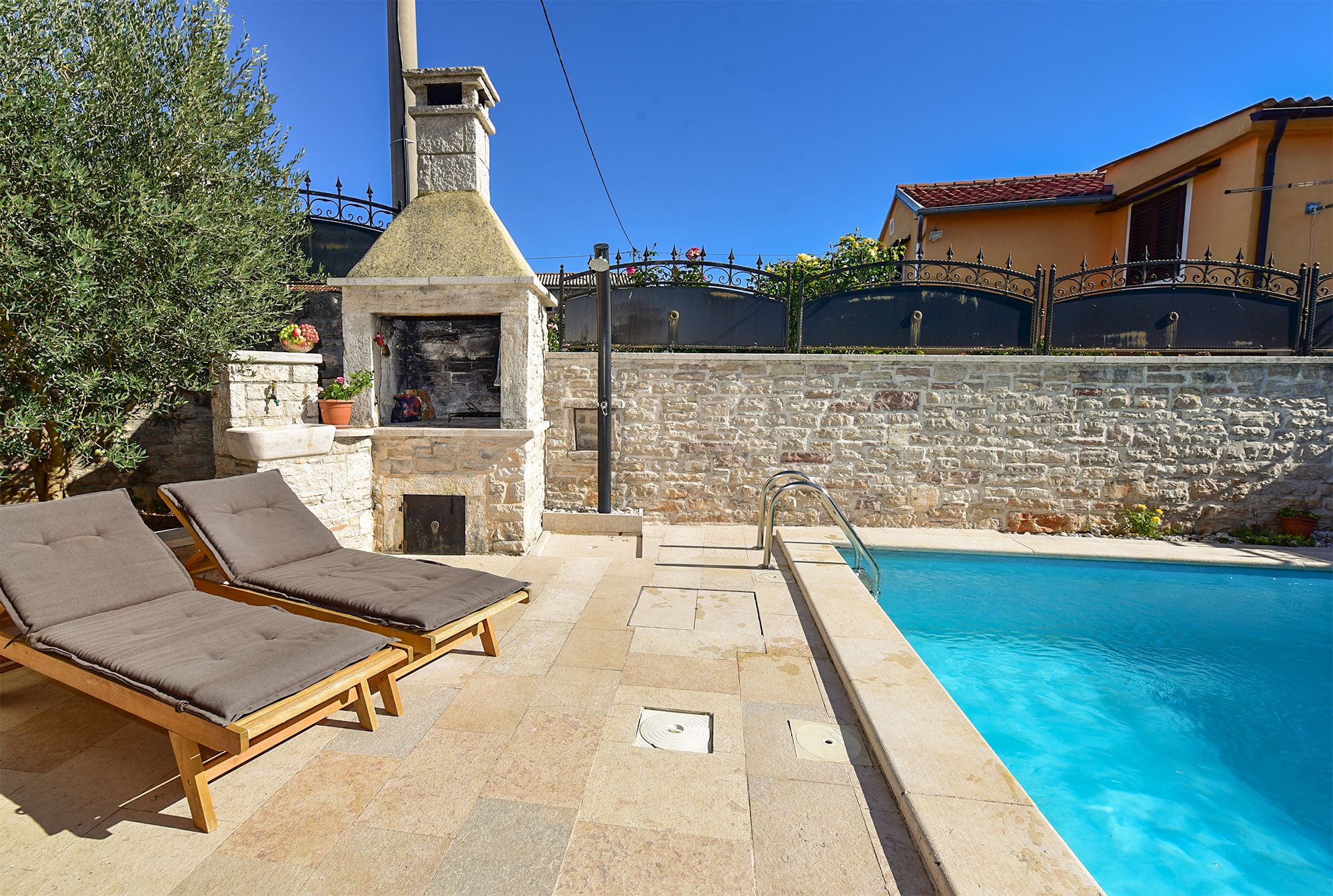 A poolside area with lounge chairs, a stone wall, and a chimney.