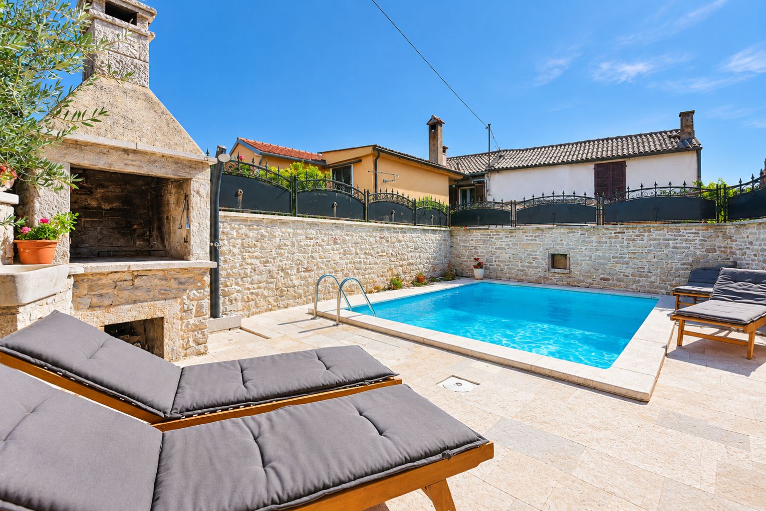 A poolside area with a stone wall, a barbecue, and lounge chairs.
