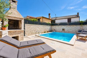 A poolside area with a stone wall, a barbecue, and lounge chairs.