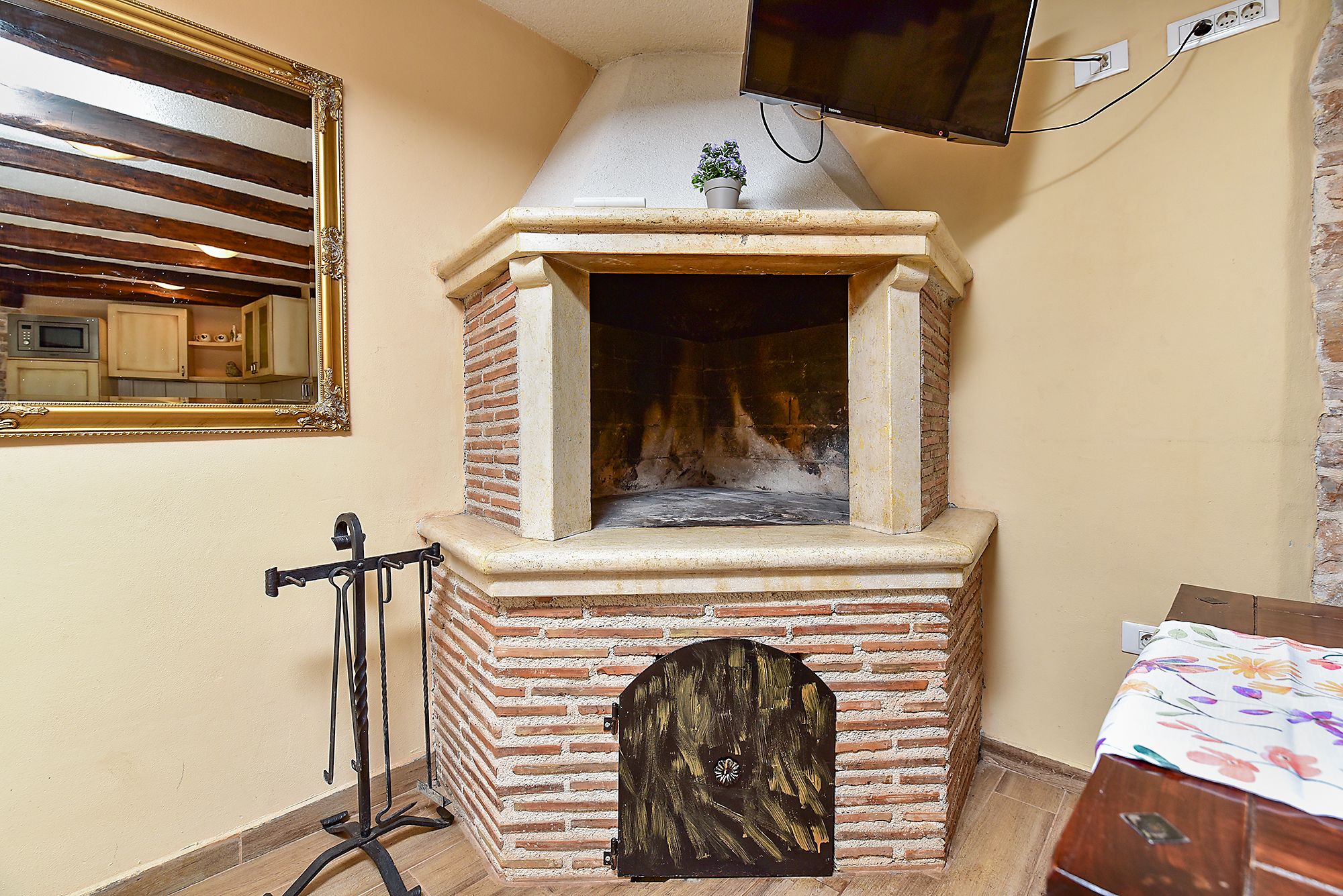 A brick oven with a chimney, a television mounted on the wall, and a small potted plant on top.
