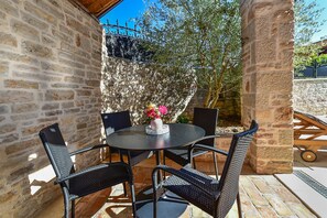 Une terrasse extérieure avec une table ronde et quatre chaises, entourée de murs en pierre et d’un arbre.