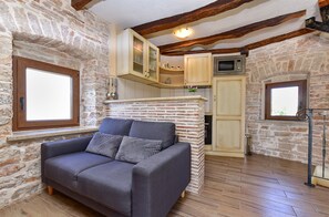 A cozy room with a sofa, wooden beams, stone walls, and a window.