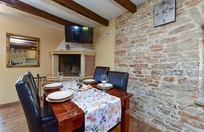 A dining area with a brick wall, a fireplace, a clock, and a television mounted above the fireplace.