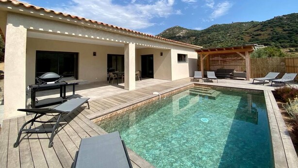 A swimming pool with lounge chairs and a barbecue area, surrounded by a wooden deck and a covered patio. - NEW VILLA **** 130 m²- Heated swimming pool - Close to L'Ile-Rousse beaches (MONTICELLO)