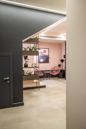 Een modern interieur met een donkergrijze deur, een roze stoel, een plantenplank en een kunstwerk aan de muur.