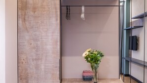 A modern room with a wooden cabinet, a small table with a vase of flowers, a brown chair, and an air conditioning unit. - Allure Boutique Hotel (Tirana)