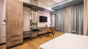 A modern hotel room with a bed, a desk with a chair, a TV, and a large window with curtains. - Allure Boutique Hotel (Tirana)