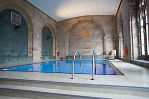 Una piscina interior con agua cristalina, rodeada de muros de piedra y arcos.