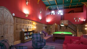Un espace intérieur chaleureux et accueillant, avec une table de billard, des meubles à motifs écossais et une bibliothèque en bois.