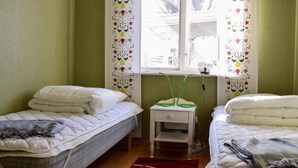 Una habitación con dos camas individuales, una mesita de noche con lámpara y una ventana con cortinas florales.