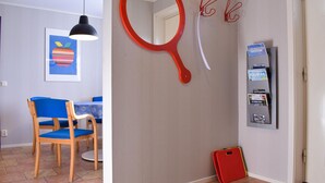 Una habitación con una silla azul, un cuadro enmarcado, un objeto rojo montado en la pared y un tablón de anuncios con revistas.