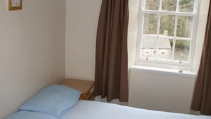 Una stanza piccola e modesta con un letto, un tavolino e una finestra con tende.