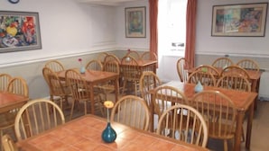 Un'area pranzo con tavoli e sedie in legno, un vaso su un tavolo e due quadri appesi alle pareti.