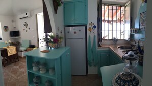 A kitchen with teal cabinets, a refrigerator, a sink, and a stove. There is a window with bars, a TV on a stand, and a table with a yellow tablecloth. - Lampedusa catatteristic dammuso sea view, 200mt distant, 180° (Lampedusa)