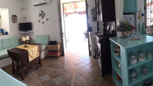 A cozy living room with a sofa, a small table with a lamp, a TV, and a kitchen area with a blue cabinet and a window with curtains. - Lampedusa catatteristic dammuso sea view, 200mt distant, 180° (Lampedusa)