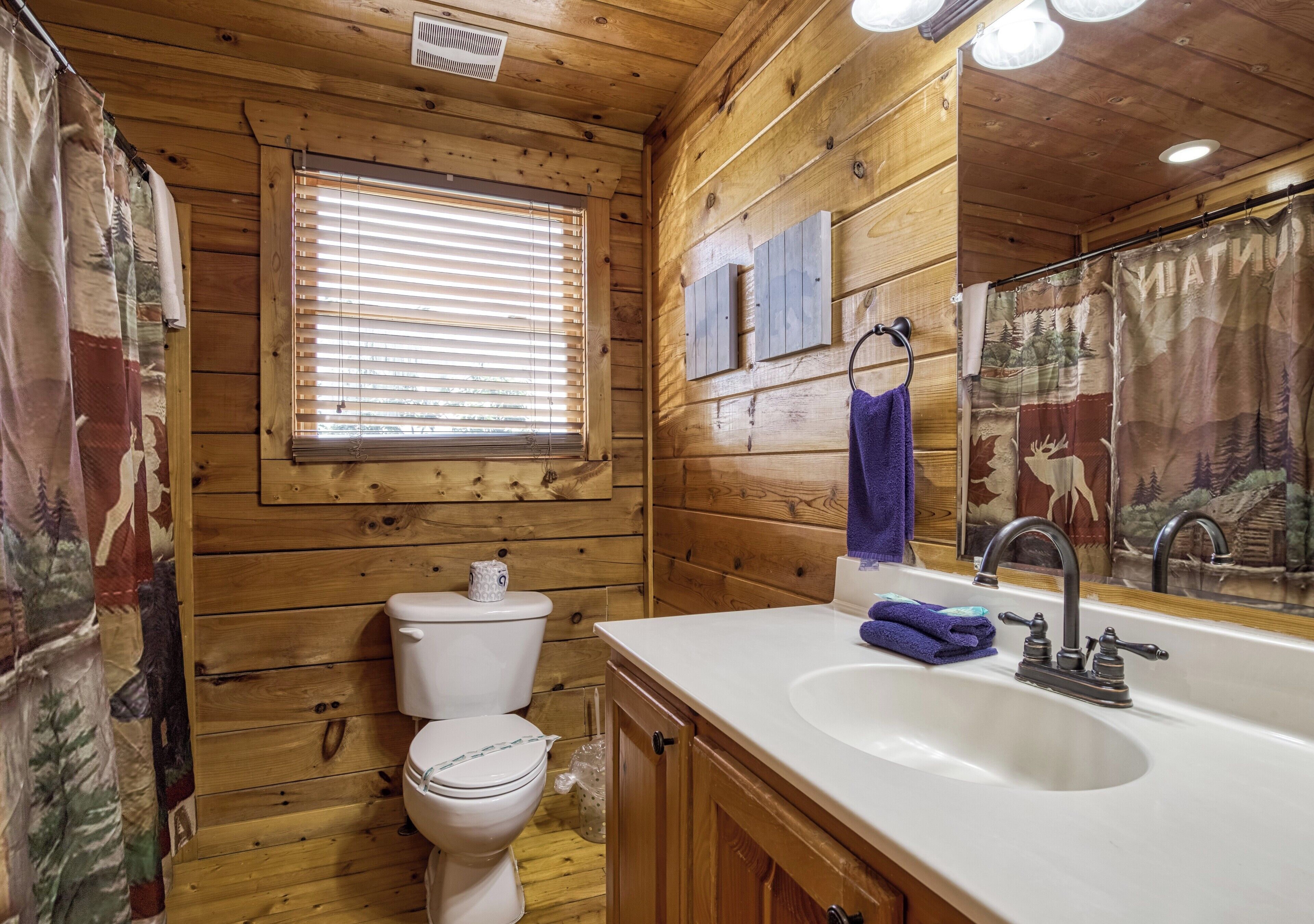 A wooden cabin bathroom with a toilet, sink, and window.
