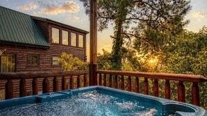 Une cabane en bois avec un bain à remous sur une terrasse, entourée d’arbres et sous un ciel dégagé.