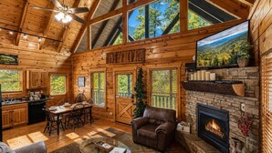 L’intérieur d’une cabane en rondins comprend un coin repas, une cheminée et de grandes fenêtres.
