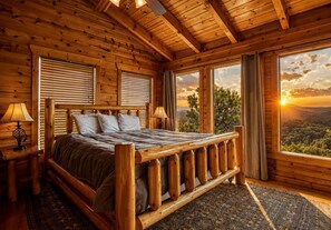 Ein Schlafzimmer einer Holzh ütte mit einem Bett, zwei Nachttischlampen, einem Fenster mit Landschaftsblick und einem gemusterten Teppich.