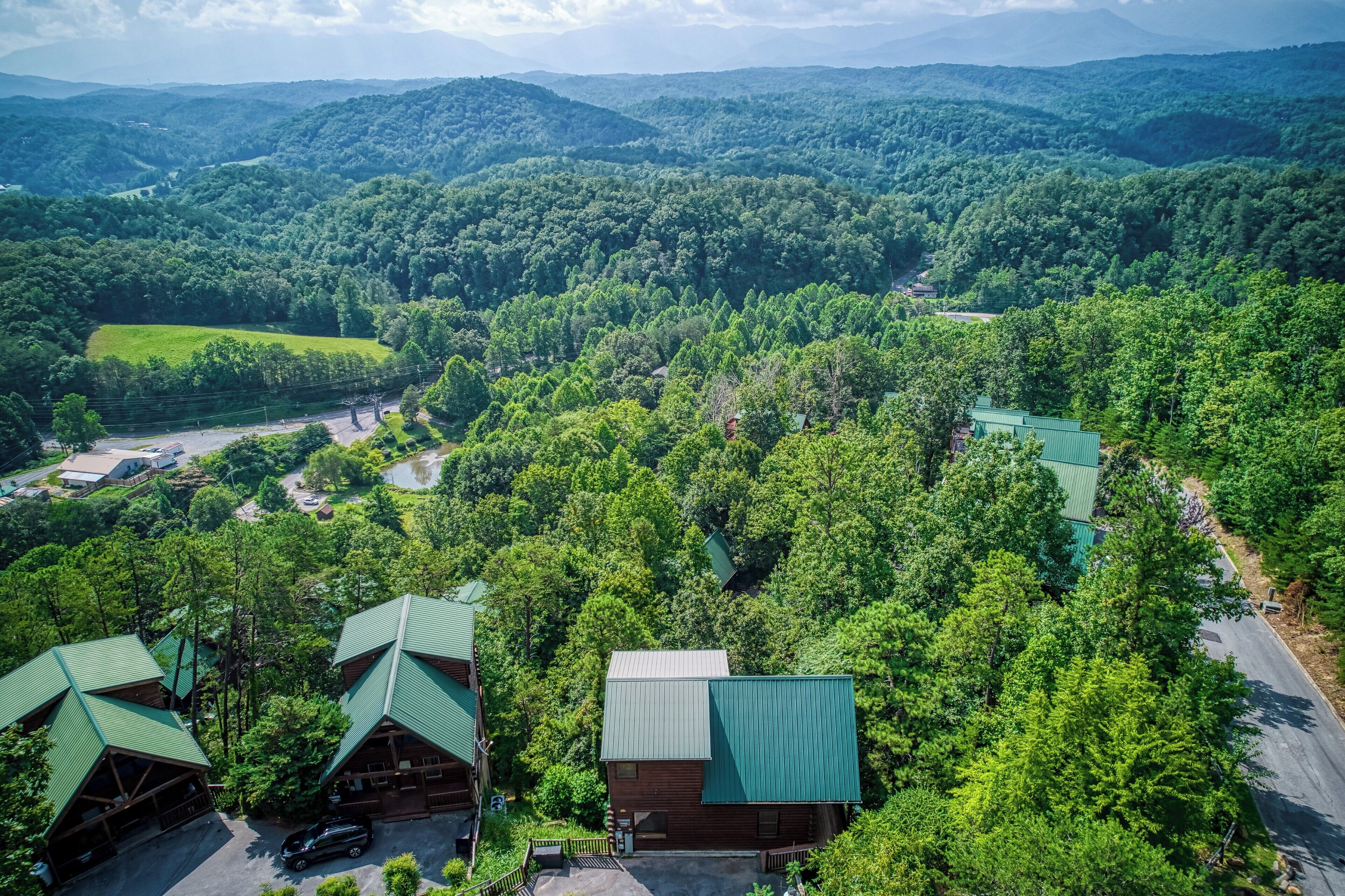 A lodge with multiple cabins, surrounded by dense forest and rolling hills.