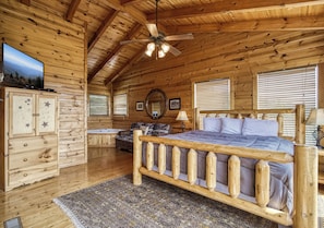 A log cabin bedroom with a wooden bed, a ceiling fan, a dresser, and a television on a cabinet. - Enchanted View, Hot Tub , FREE tickets, Theater Room, Game Room!!! (Sevierville)