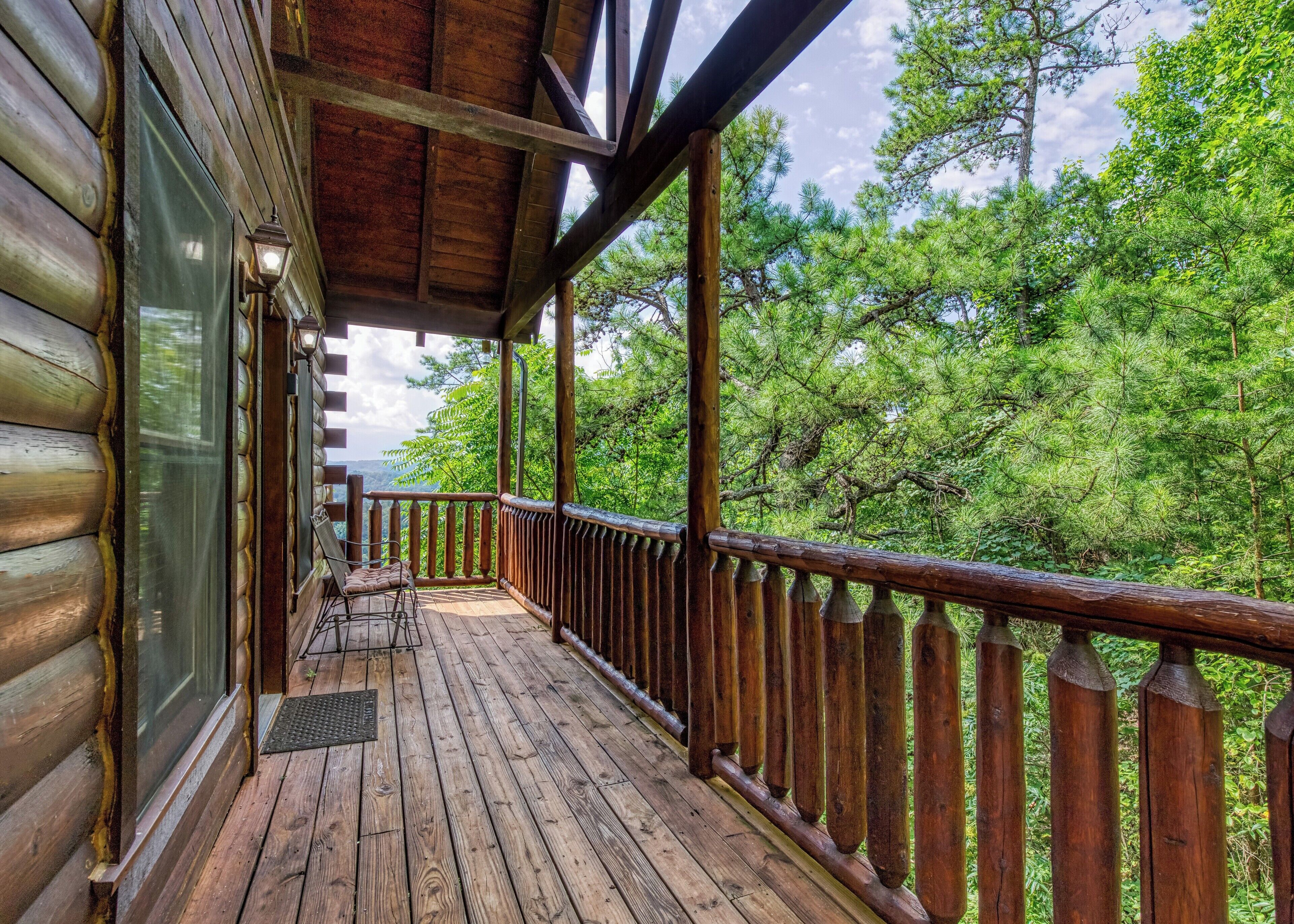 Une terrasse en bois avec une rambarde, une chaise et une vue sur les arbres.